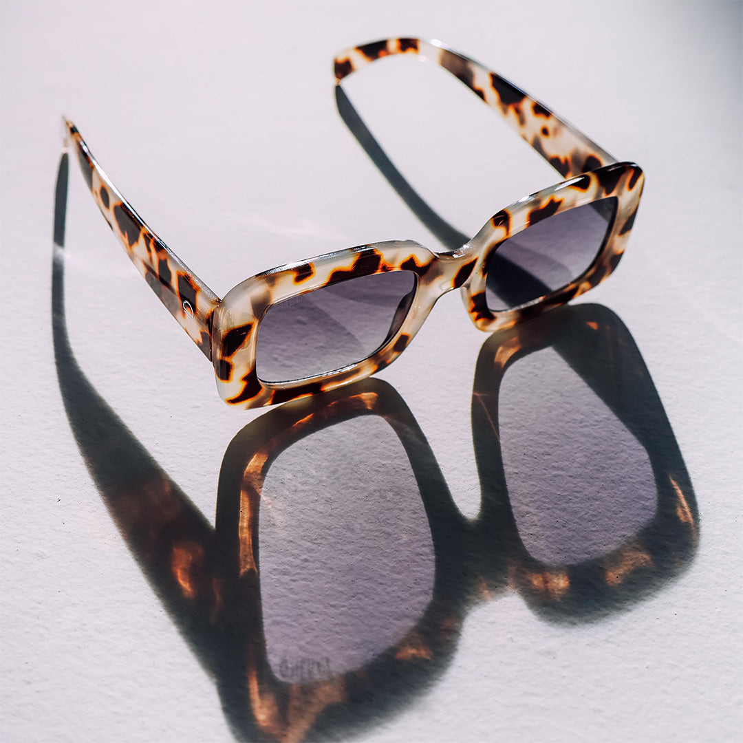 Holiday Tortoise Shell Rectangle Womens Blue Lens Sunglasses laid out on the ground showing a reflection