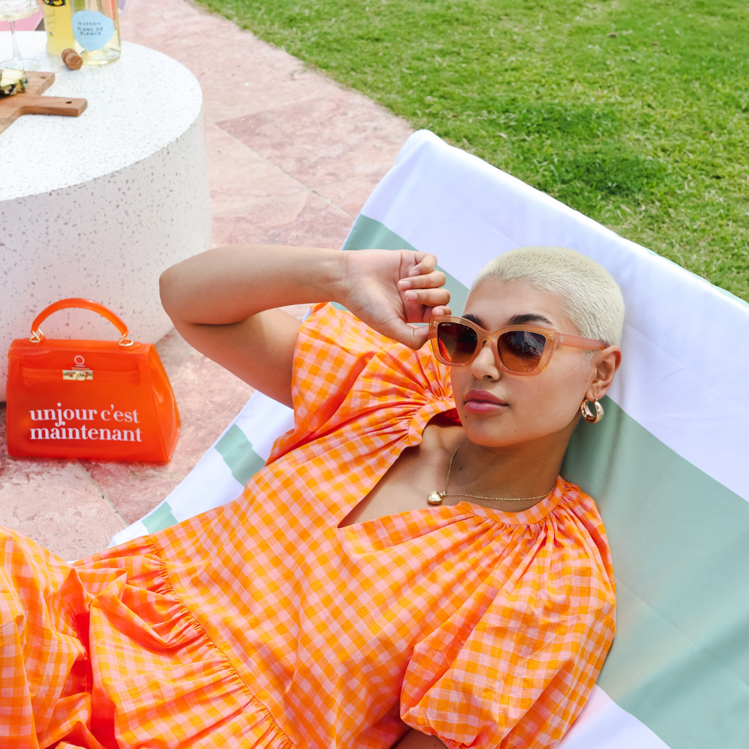 Female model wearing Beach Please - Brown Brown while lying on a pool lounge chair